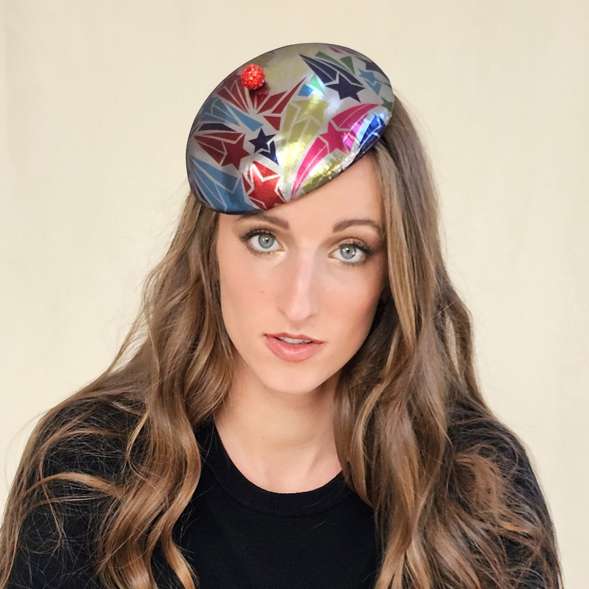 Close-up of silver beret with multicolour stars and a red globe on model.