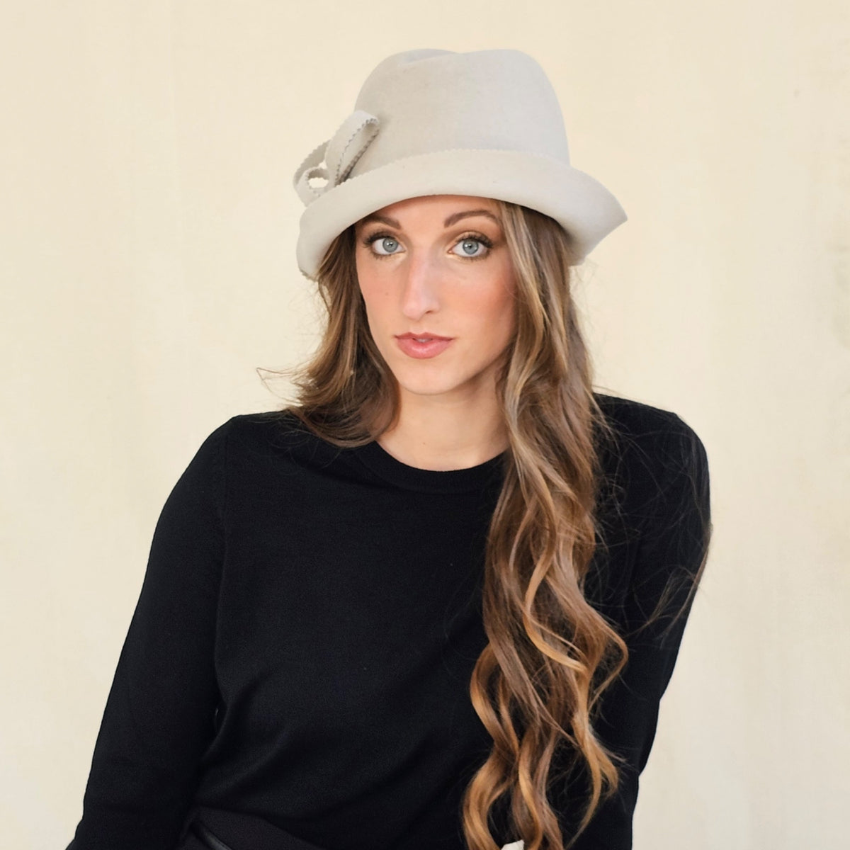 Stone felt trilby with an asymmetric brim and loop bow, worn on a
model.
