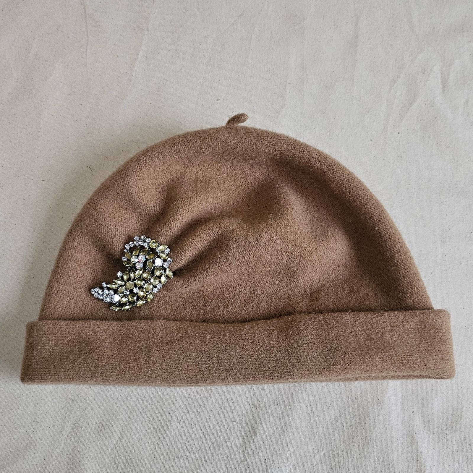 Tan wool beanie with beautiful brooch, top view.