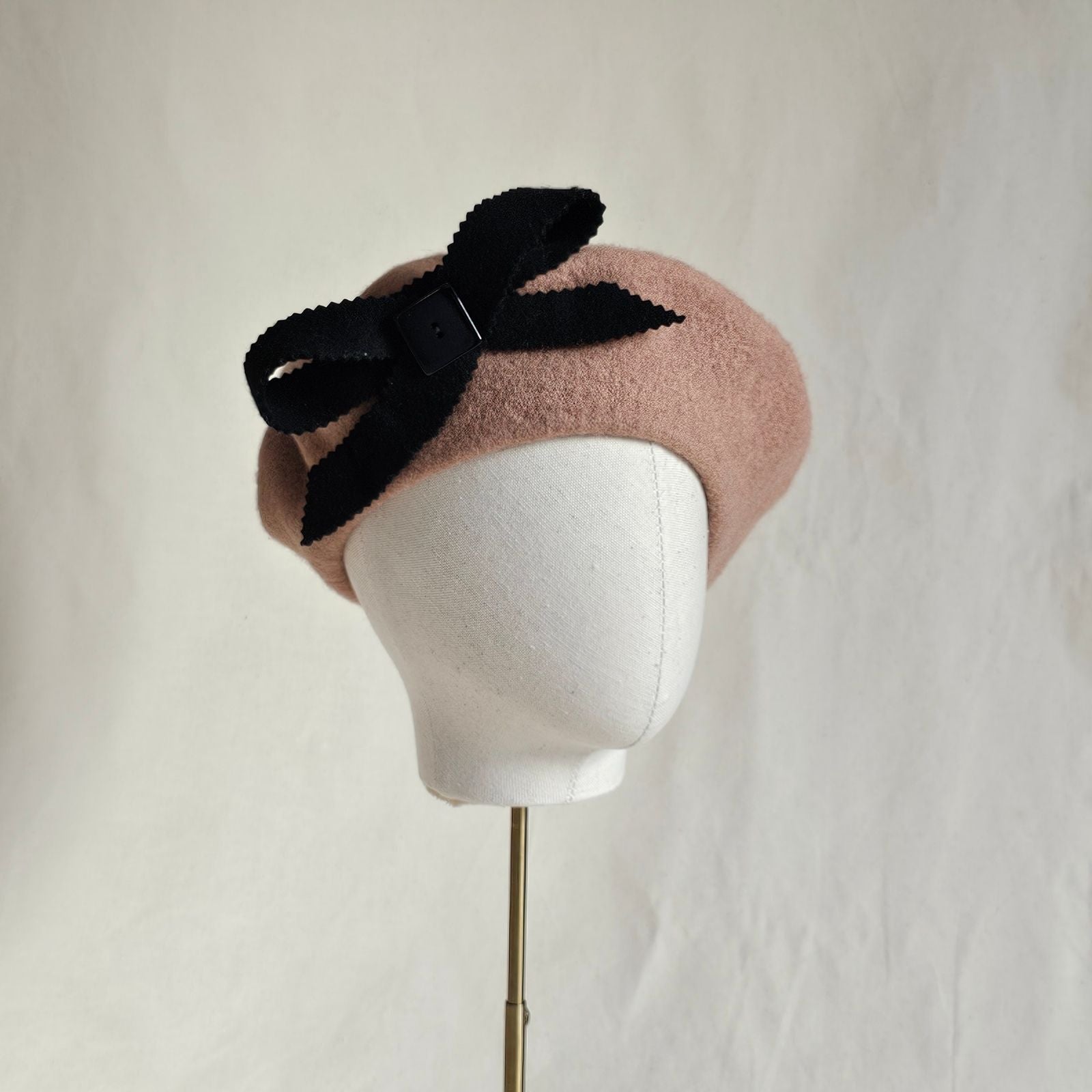 Tan wool beret with elegant black bow embellishment, angle view.