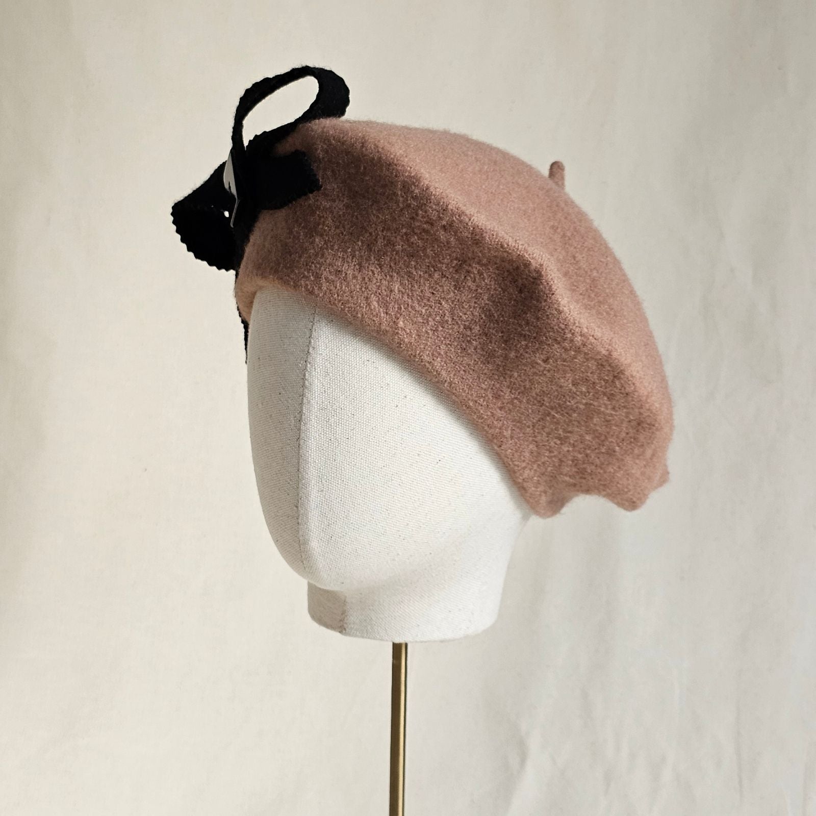 Tan wool beret with black bow embellishment, left view.