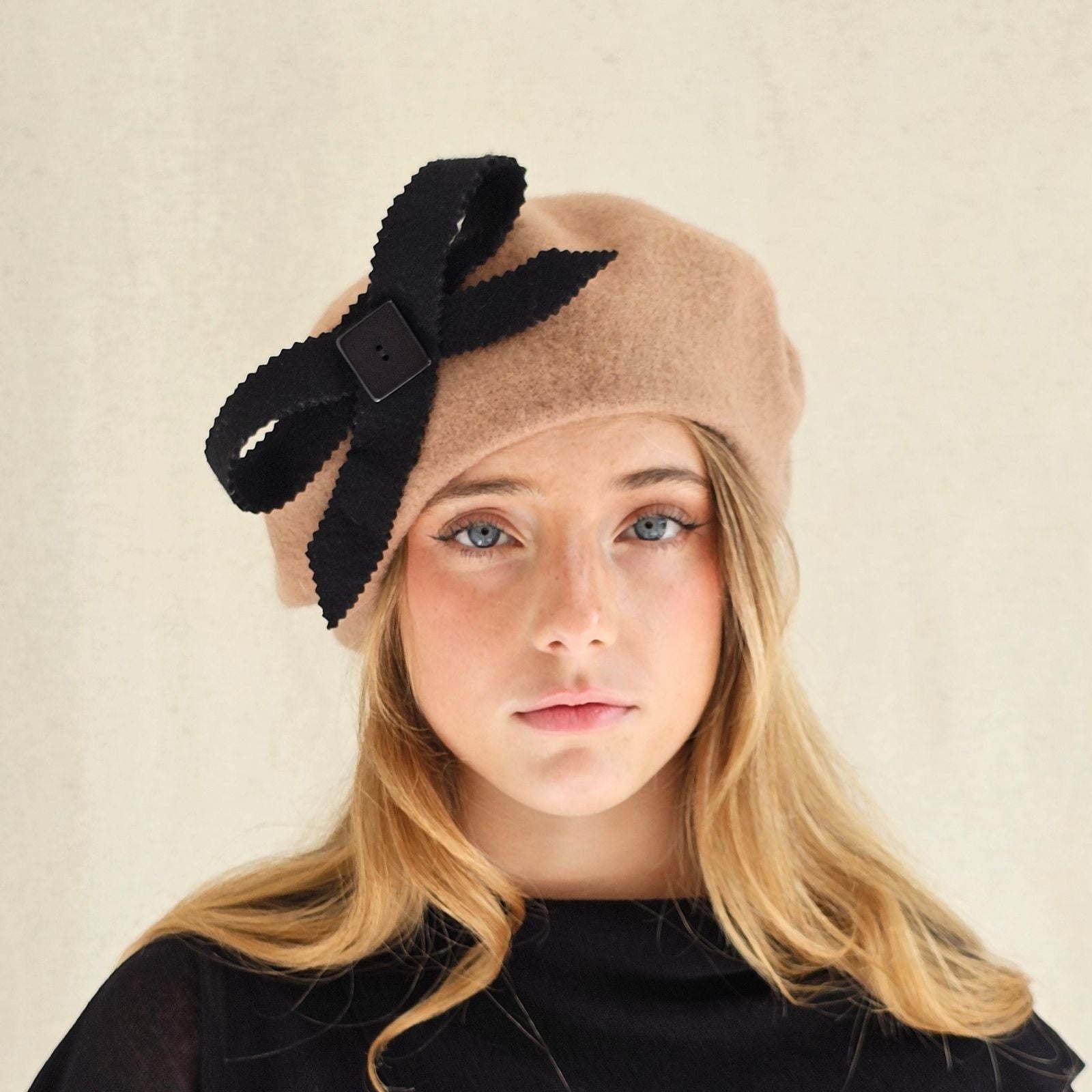 Tan wool beret with black bow embellishment, front view.