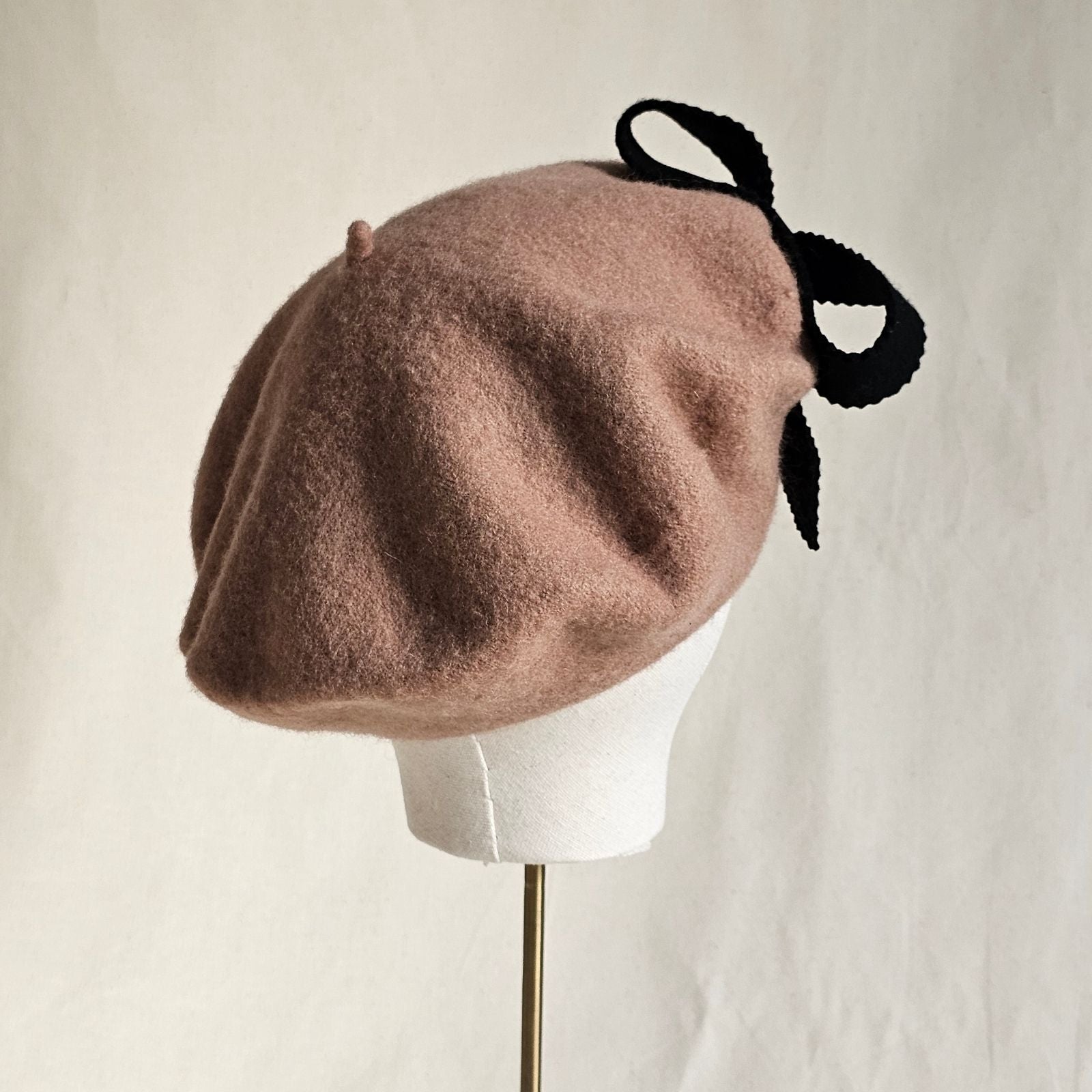 Tan wool beret with black bow embellishment, rear view.