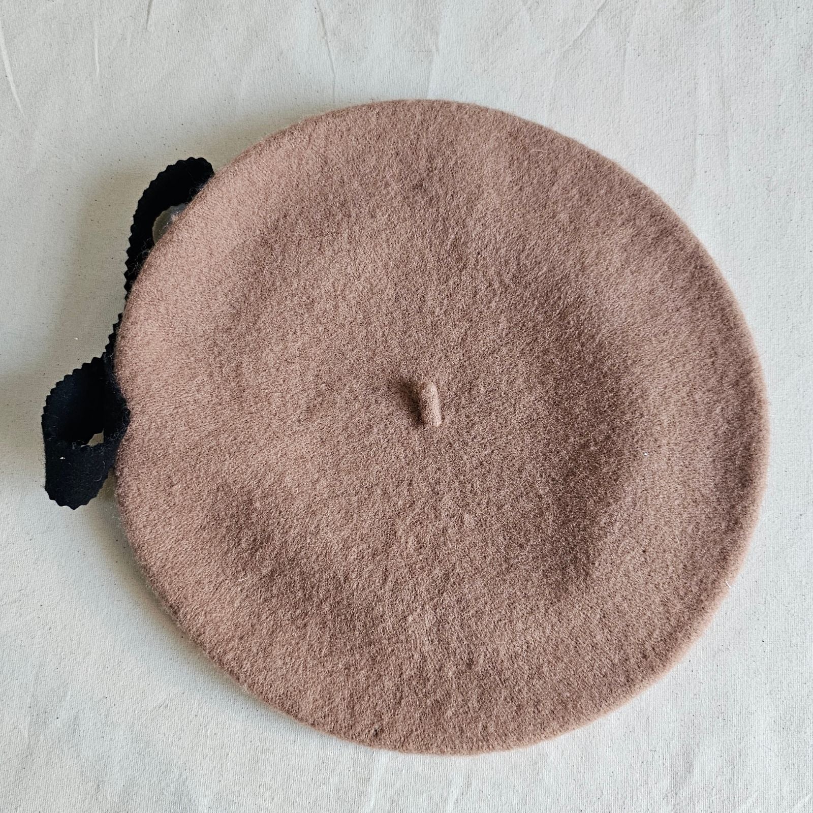 Tan wool beret with black felt bow embellishment, top view.