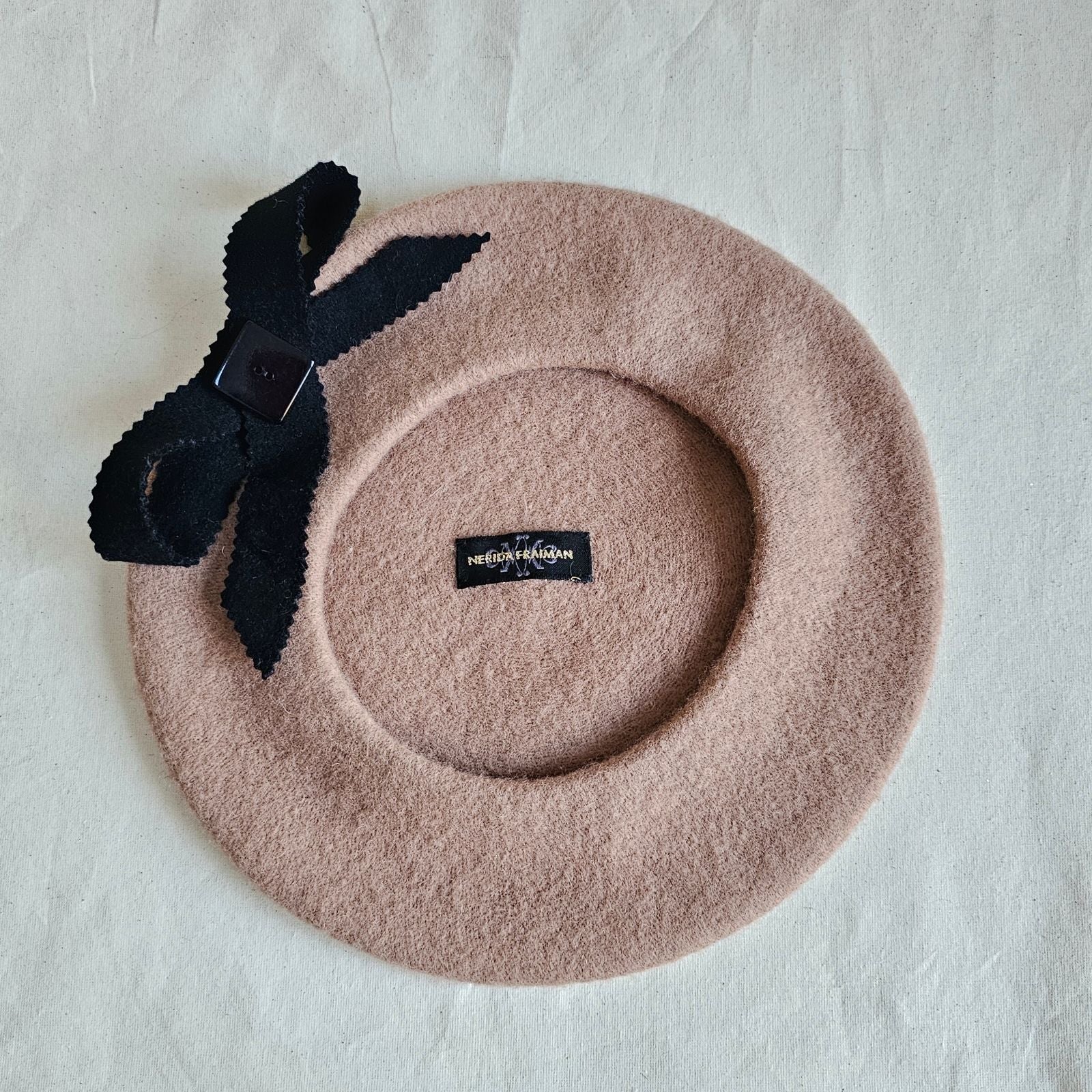 Tan wool beret with black bow embellishment, underside view.