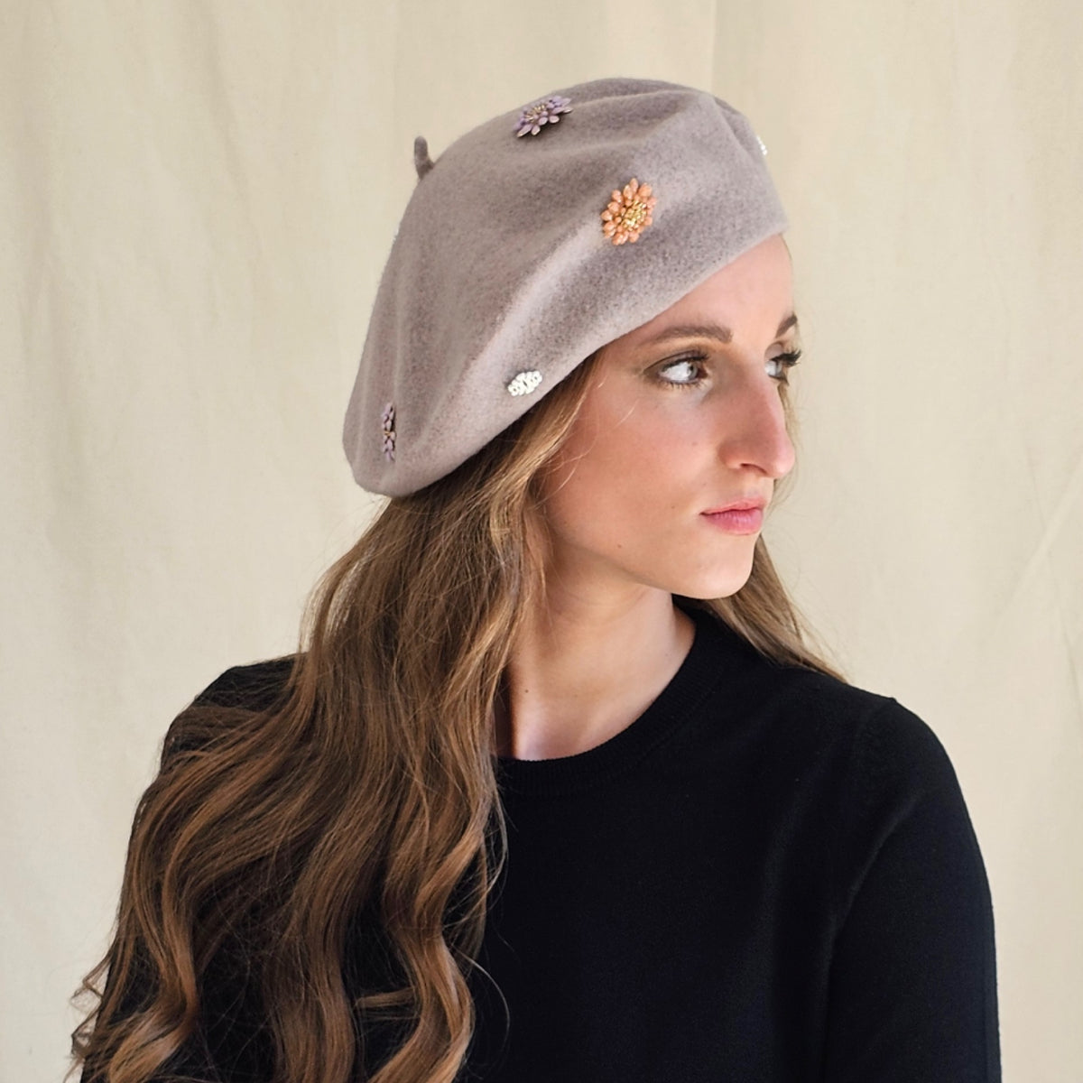 Side view of taupe wool beret showing flower and monogram
details.