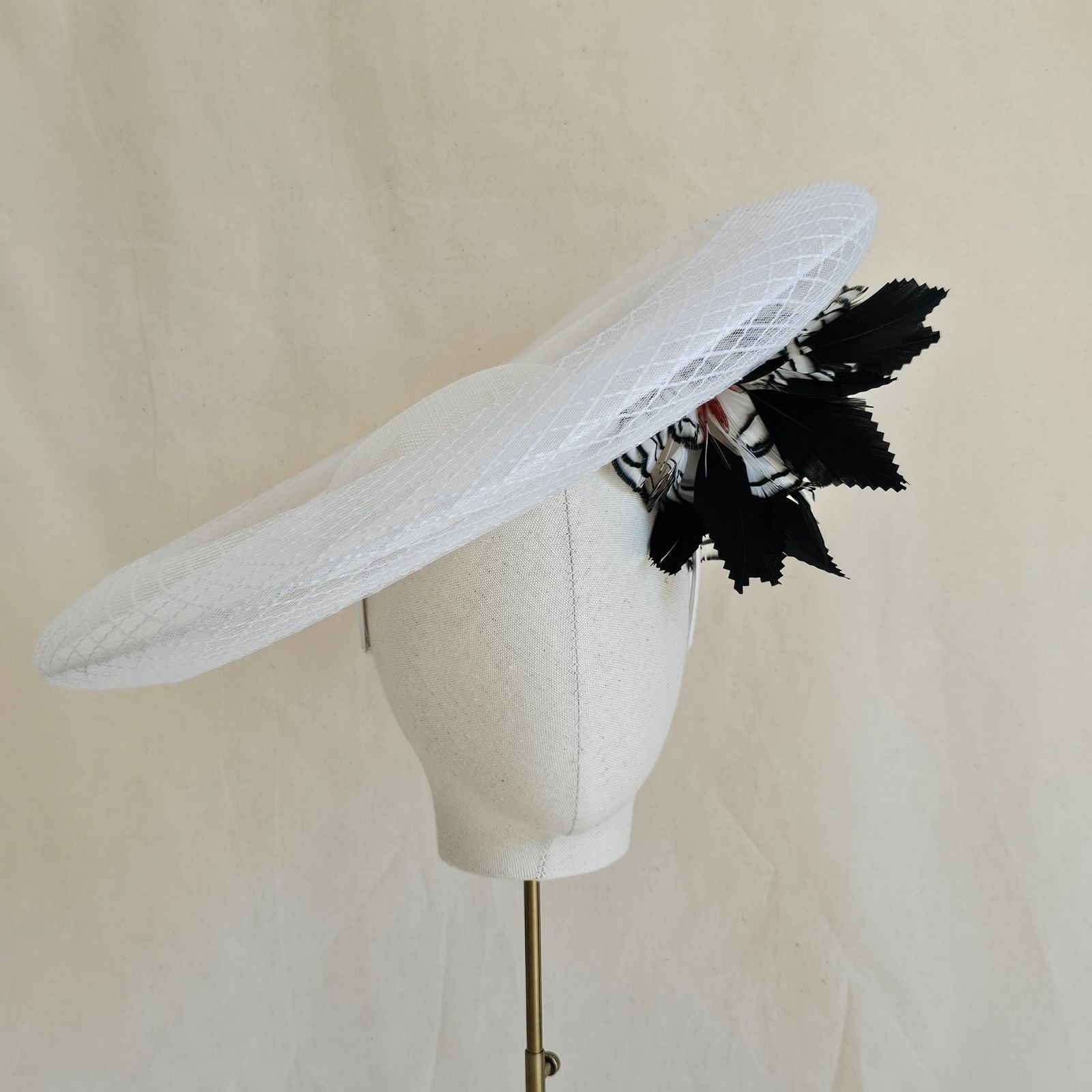 White disc hat with check crin surround and black and white feather flower under brim, front view.