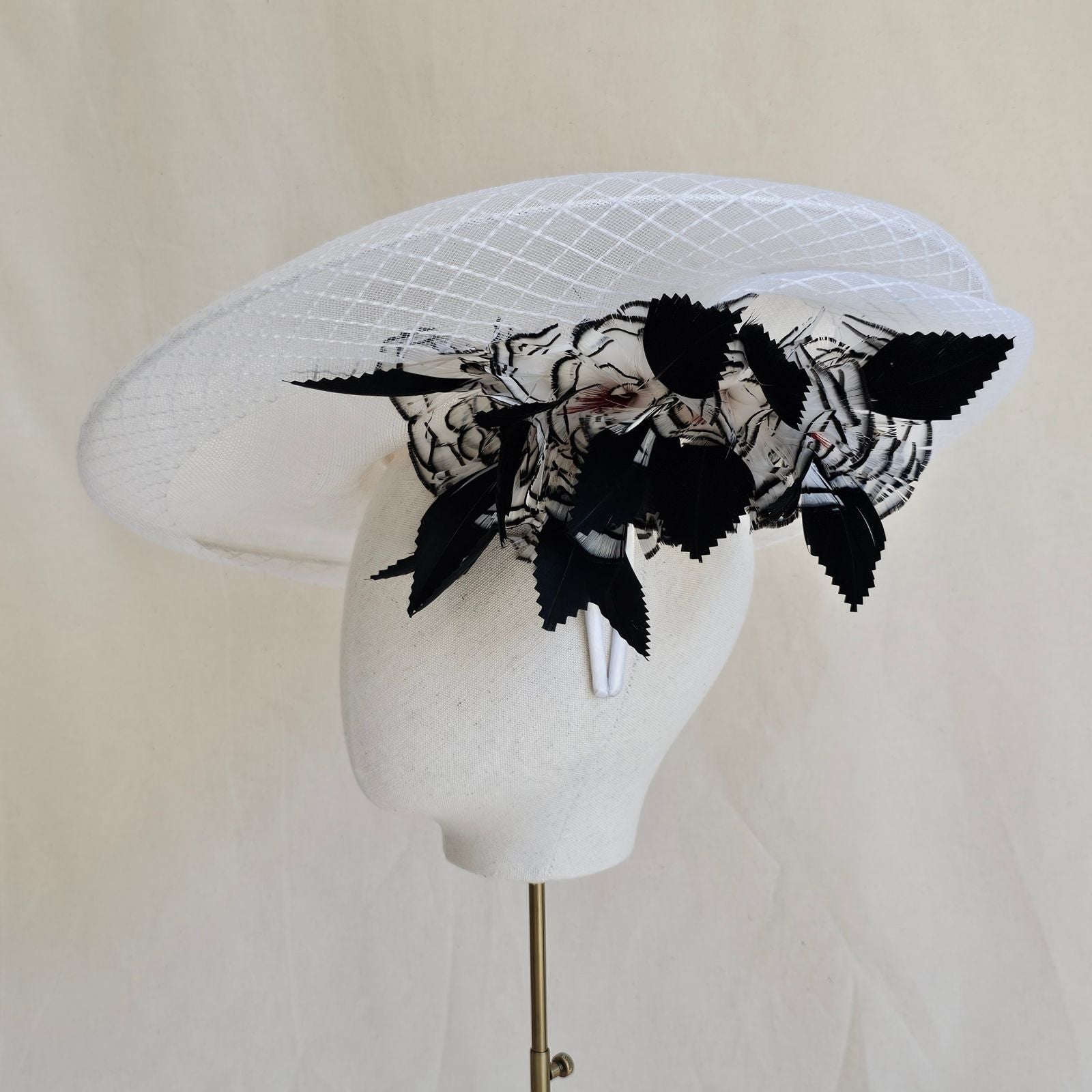 White disc hat with check crin surround and black and white feather flower under brim, side view.